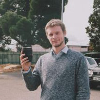 Kristian Leadbeater, bearded, holds up a paper cup of coffee