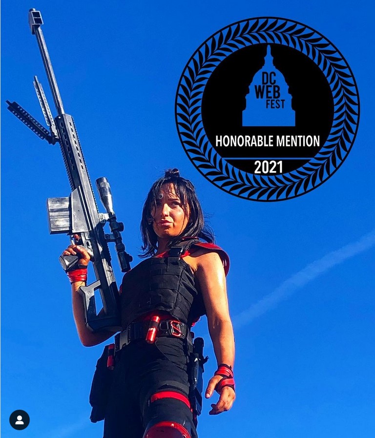 Picture of Lisa standing holding a huge gun, with a sign behind her saying, 